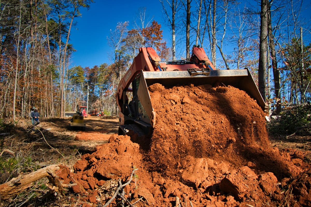 Compact track loader carrying a bucket of dirt on a wooded site